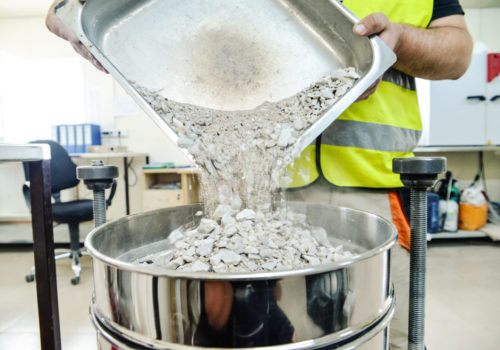 On site road testing laboratory. Placing sample of gravel into a silver container. Preparation step - pouring sample of a layer of soil